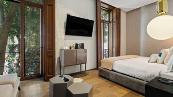 A modern bedroom with a bed, a TV, a desk, and a balcony with a view of trees.