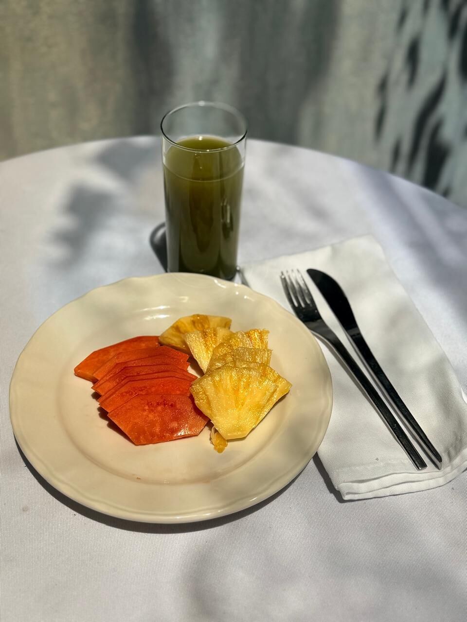 A plate with sliced fruits and a glass of green drink on a white table.