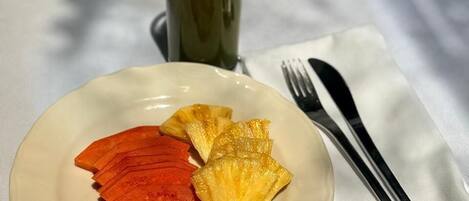 A plate with sliced fruits and a glass of green drink on a white table.