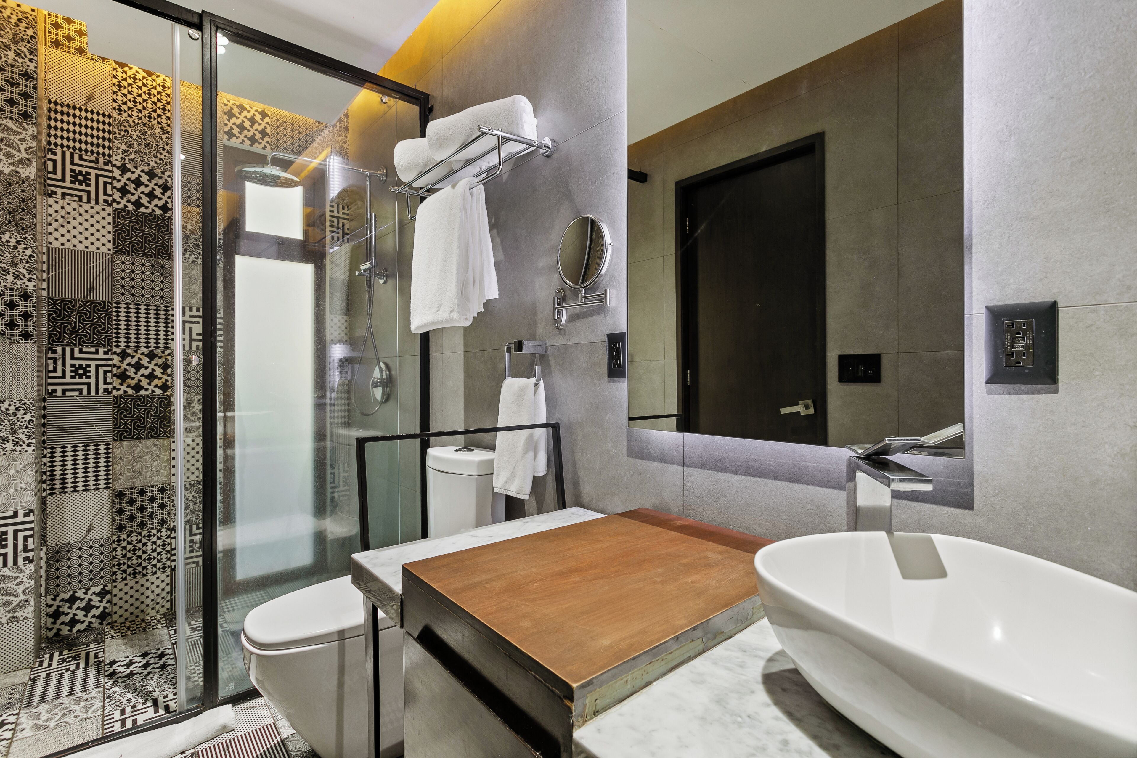 A modern bathroom with a glass shower enclosure, a wooden vanity, a large freestanding sink, and patterned tiles.