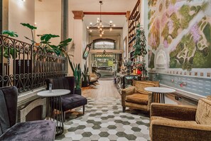 Eine Hotelhalle mit Schachbrettmuster-Boden, Sitzbereichen, einer Treppe und einem großen Wandgemälde.