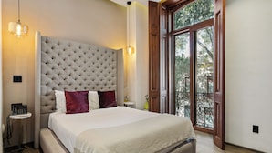 Une chambre à coucher avec une tête de lit capitonnée, un téléphone sur la table de chevet, une fenêtre donnant sur un beau paysage et une porte menant à l’extérieur.