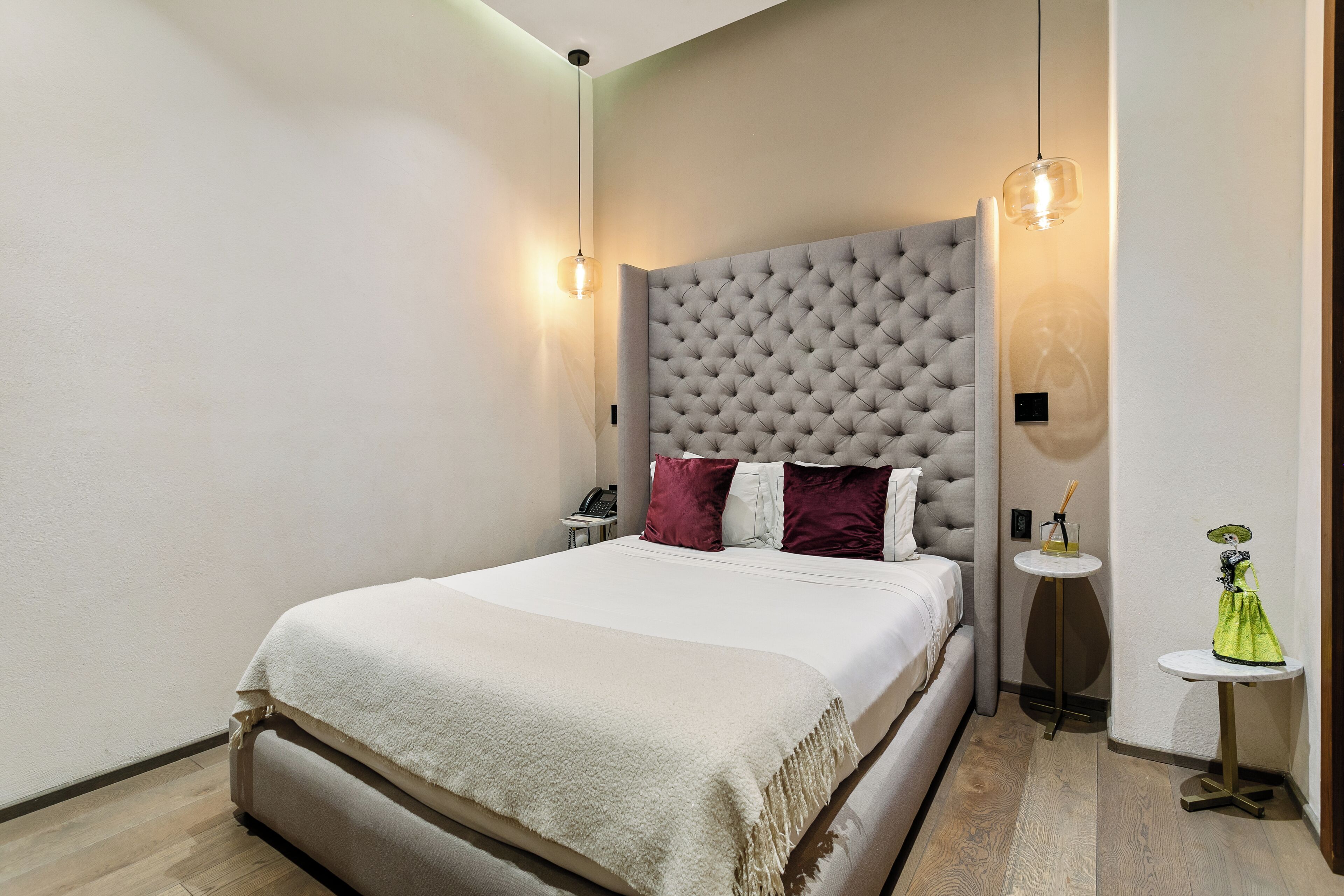Un dormitorio con una cama grande, cabecera capitonada, mesitas de noche y una pequeña mesa redonda con un objeto decorativo.