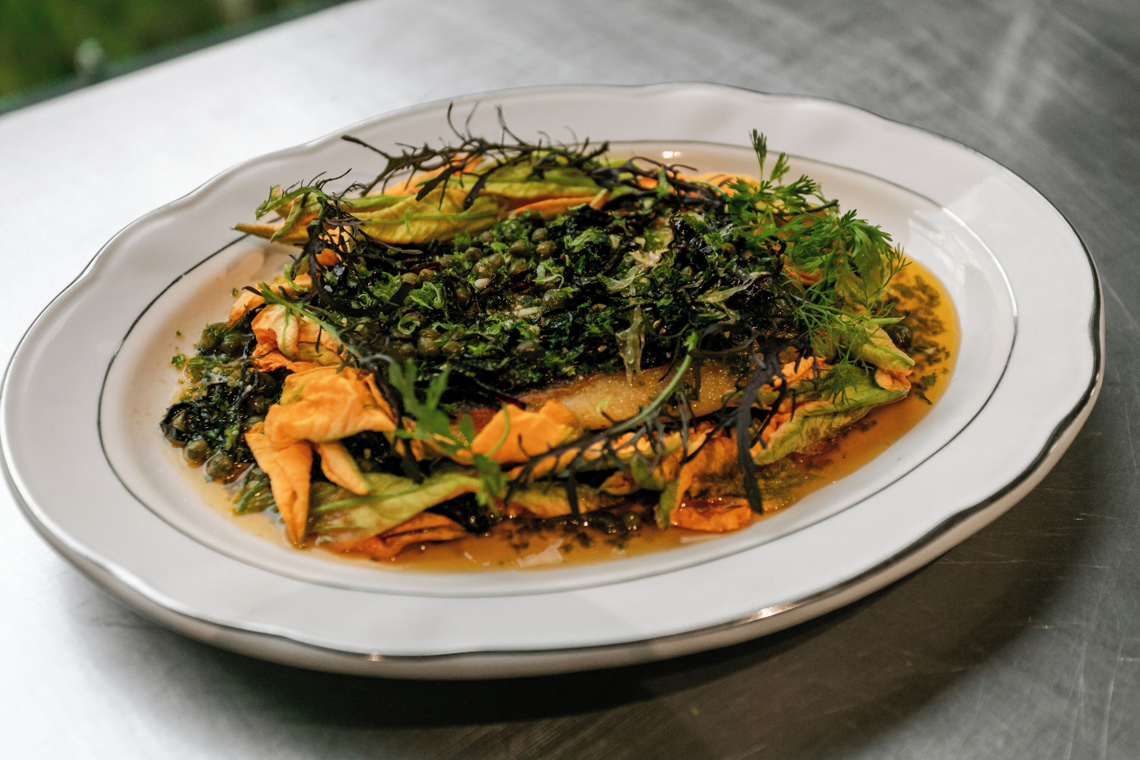 A white plate with a dish of food, possibly a stir-fry, garnished with greens and herbs.