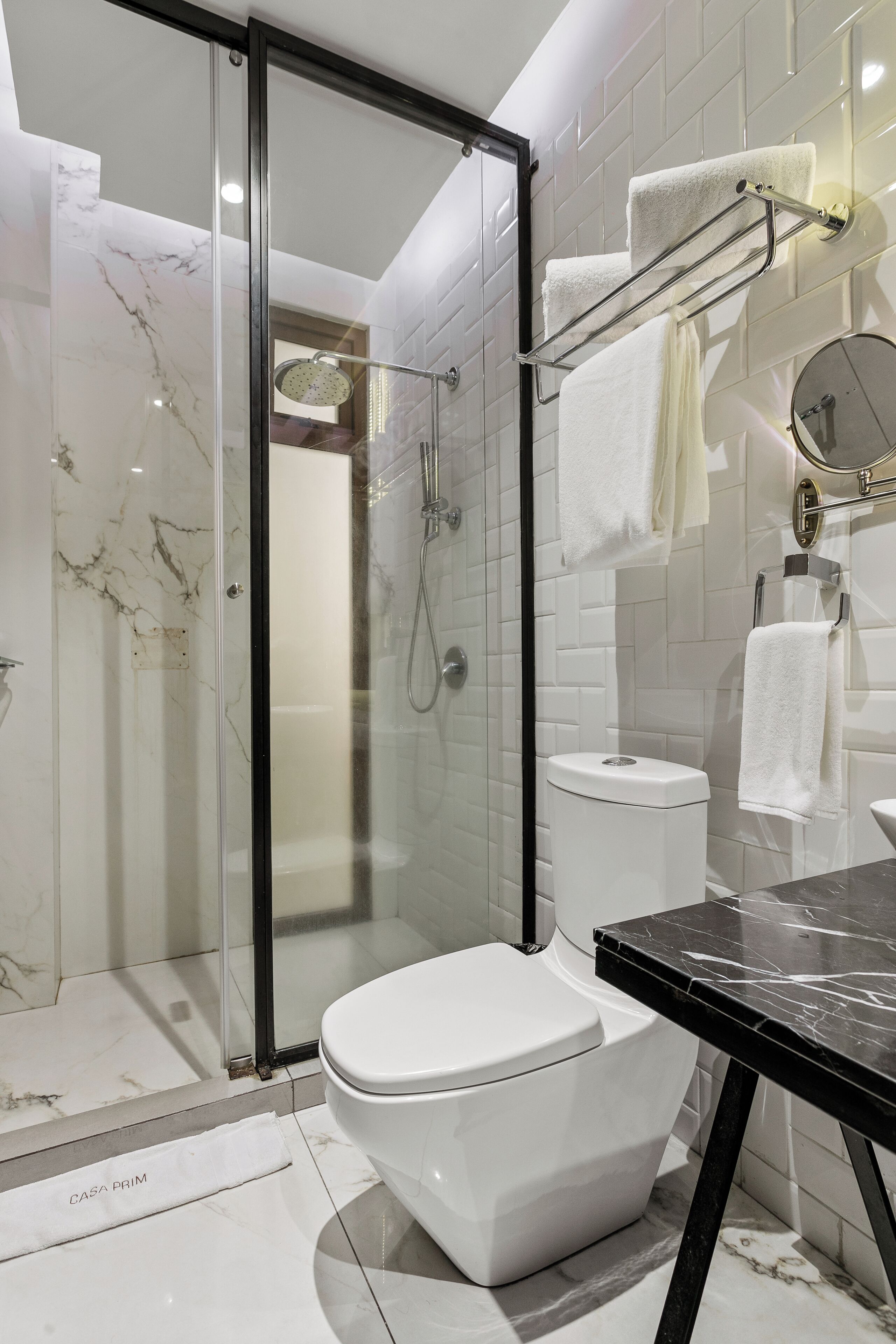 A modern bathroom with a glass-enclosed shower, a white toilet, and a black marble countertop.