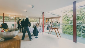 Un espace intérieur aménagé avec des tables et des chaises, un grand saladier posé sur une table, et un balcon agrémenté de plantes.