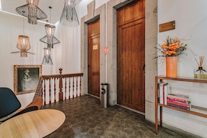 A lobby with a wooden staircase, a trash bin, a bookshelf with books, and a framed picture on the wall.