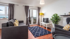 Ein modernes Wohnzimmer mit einer Couch, einem Sessel und einem Fernseher auf einem weißen Schrank.