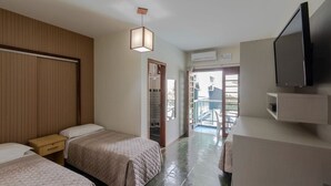 Une chambre d’hôtel avec deux lits, une tête de lit en bois, un téléviseur à écran plat, un petit bureau et un balcon avec vue.