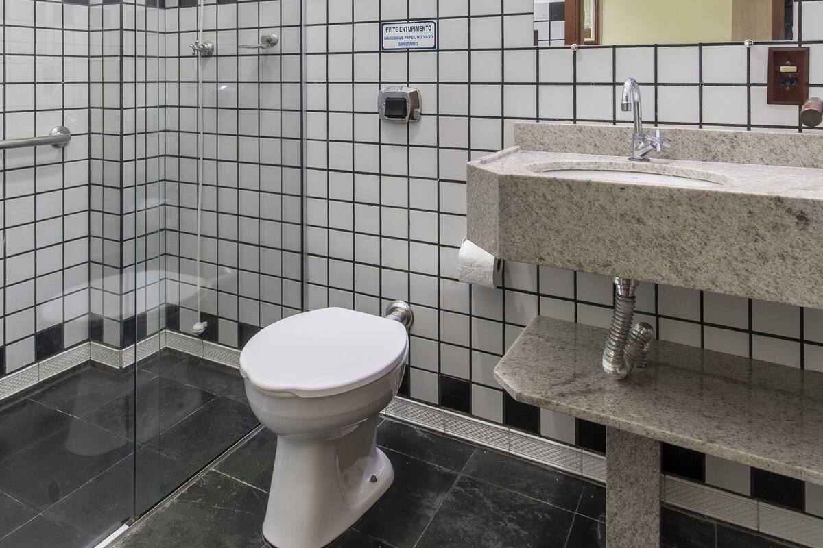 A bathroom with a glass shower enclosure, a white toilet, a sink with a marble countertop, and a tiled wall with a black and white pattern.