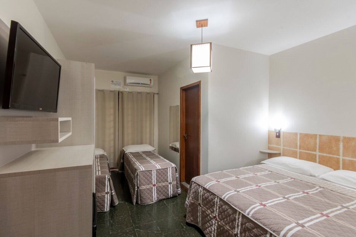 A hotel room with two beds, a television, an air conditioning unit, and a small table.
