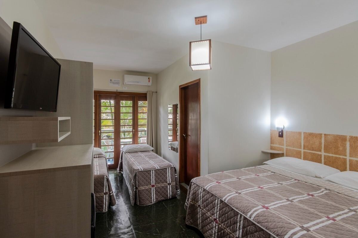 Une chambre d’hôtel avec deux lits, une télévision, un bureau et une fenêtre donnant sur un espace verdoyant.