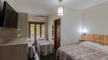 A hotel room with two beds, a TV, a desk, and a window with a view of greenery.