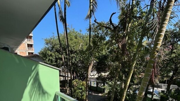 Un balcon avec une table et des chaises, donnant sur un jardin agrémenté de palmiers et sur un bâtiment visible au loin.