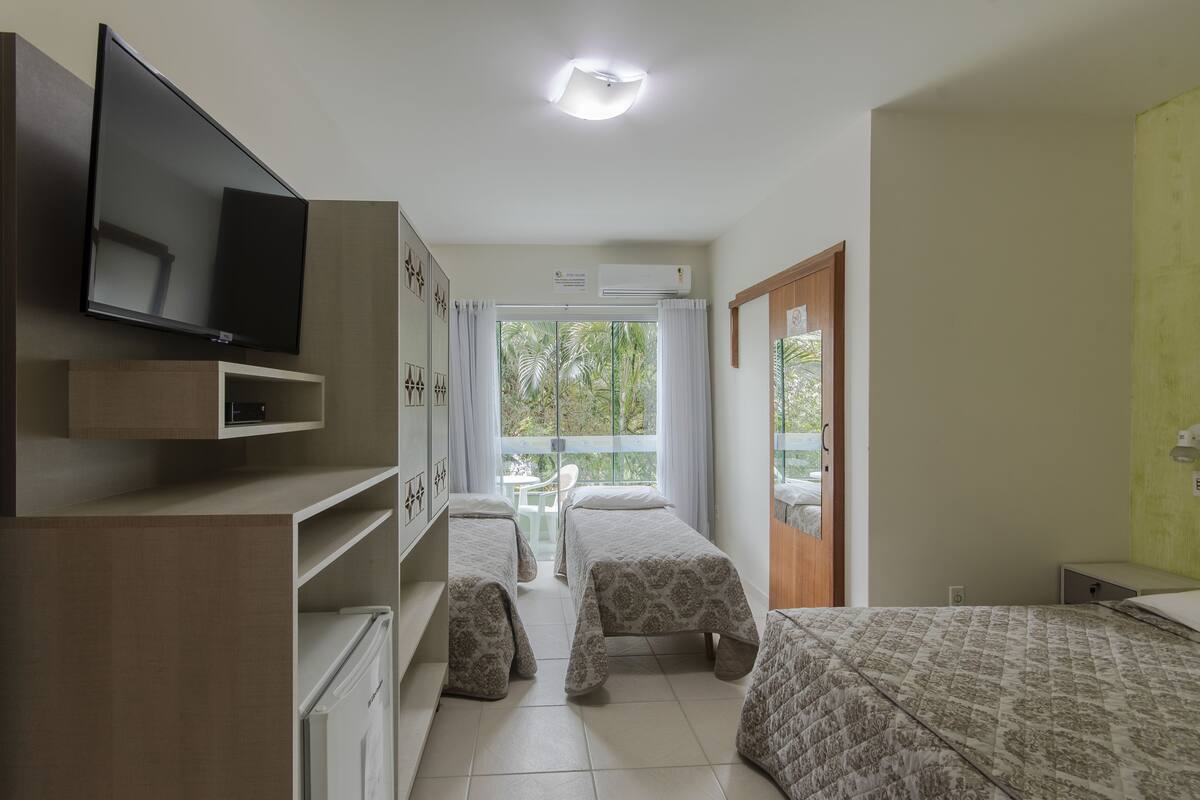 A bedroom with two beds, a TV, a desk, and a window with curtains.