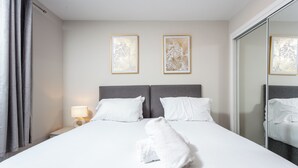 A hotel room with a large bed, two pillows, a nightstand with a lamp, and two framed wall art pieces. - Harbour House - Donnini Apartments (Ayr)