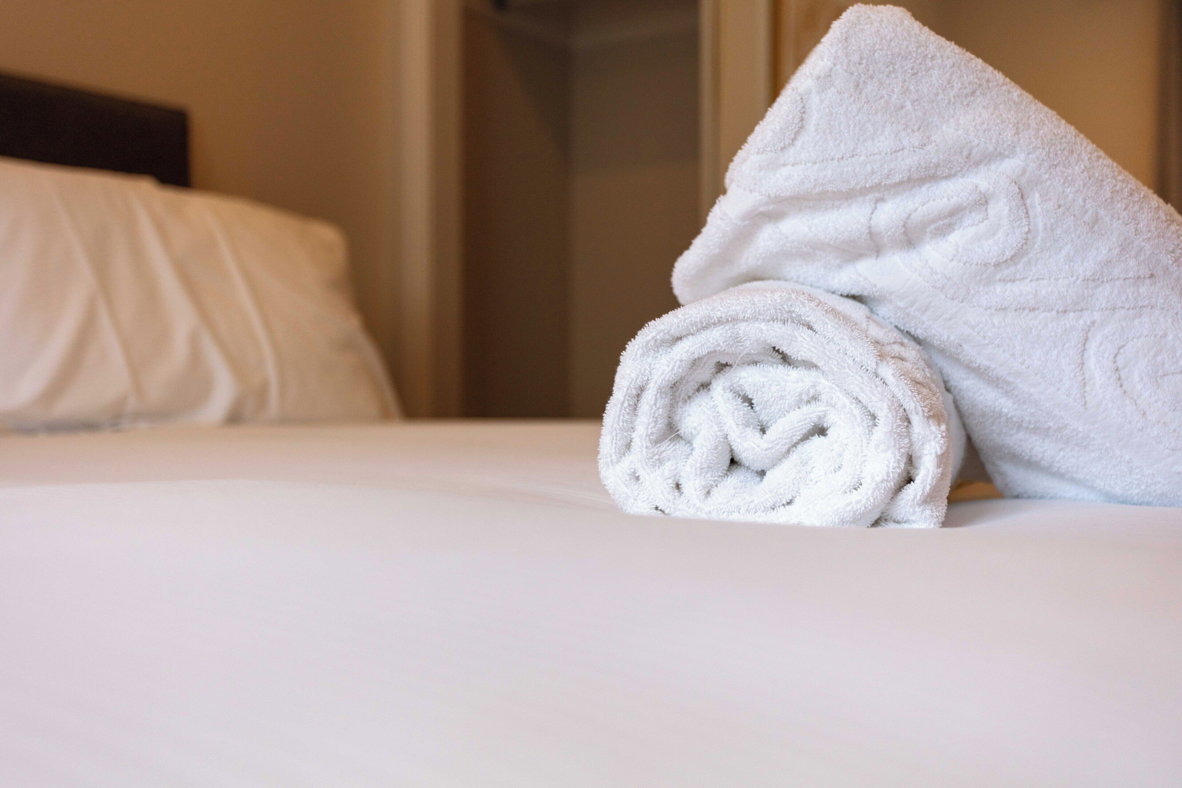 A neatly made bed with a rolled white towel on the side.