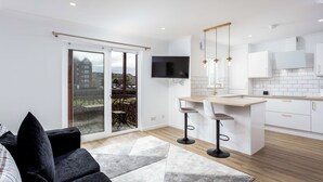 A modern kitchen with a large island, bar stools, and a TV mounted above the island. - Harbour House - Donnini Apartments (Ayr)