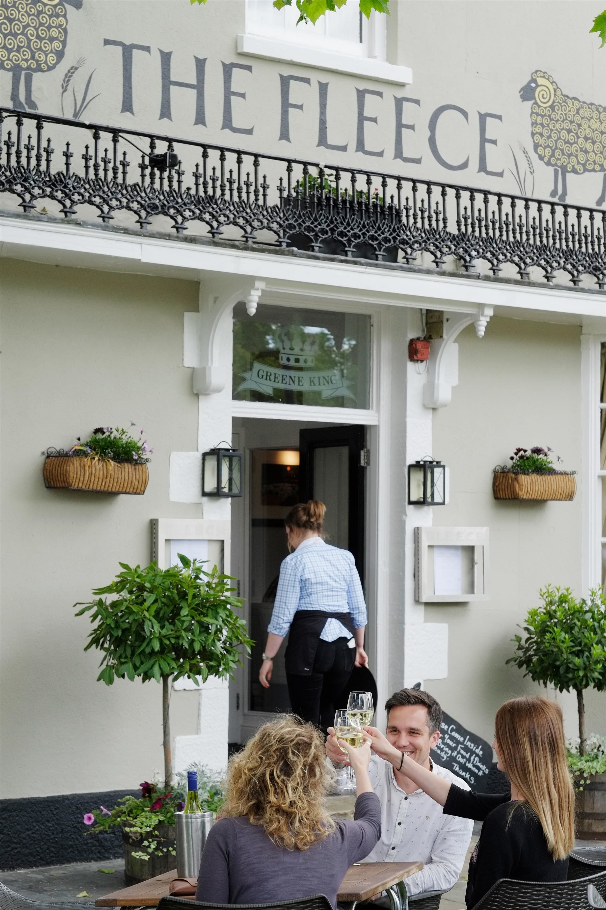 Un restaurante llamado "The Fleece" con terraza y cestas decorativas de flores.