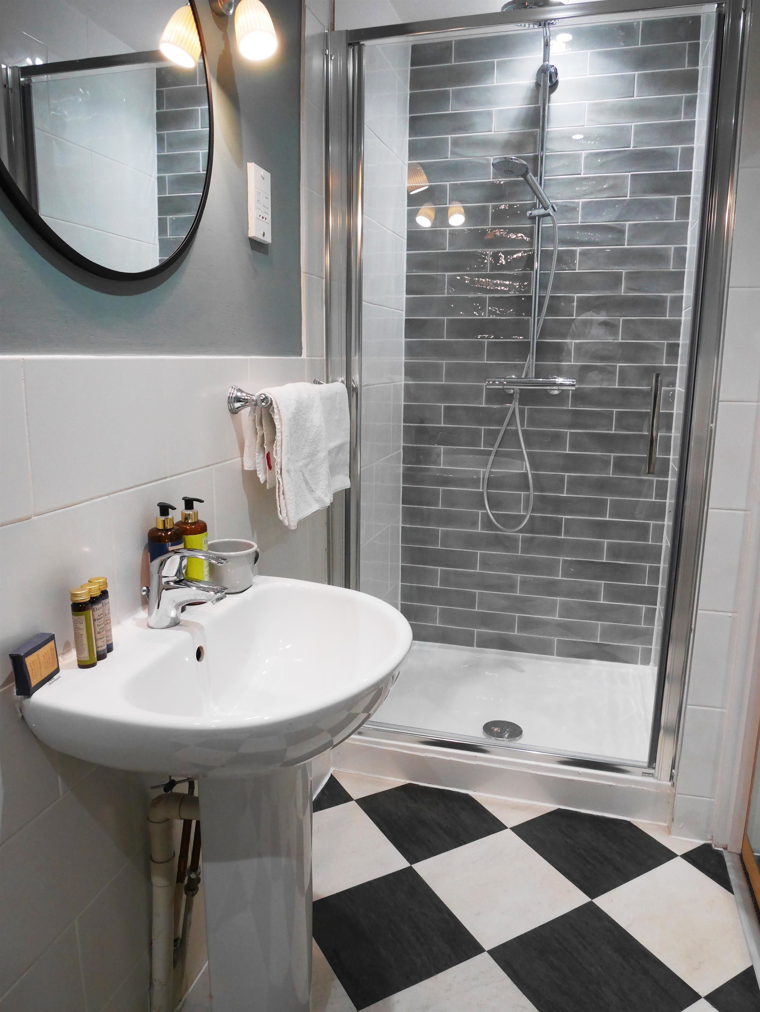 A bathroom with a glass-enclosed shower, a white sink, and a checkered floor.