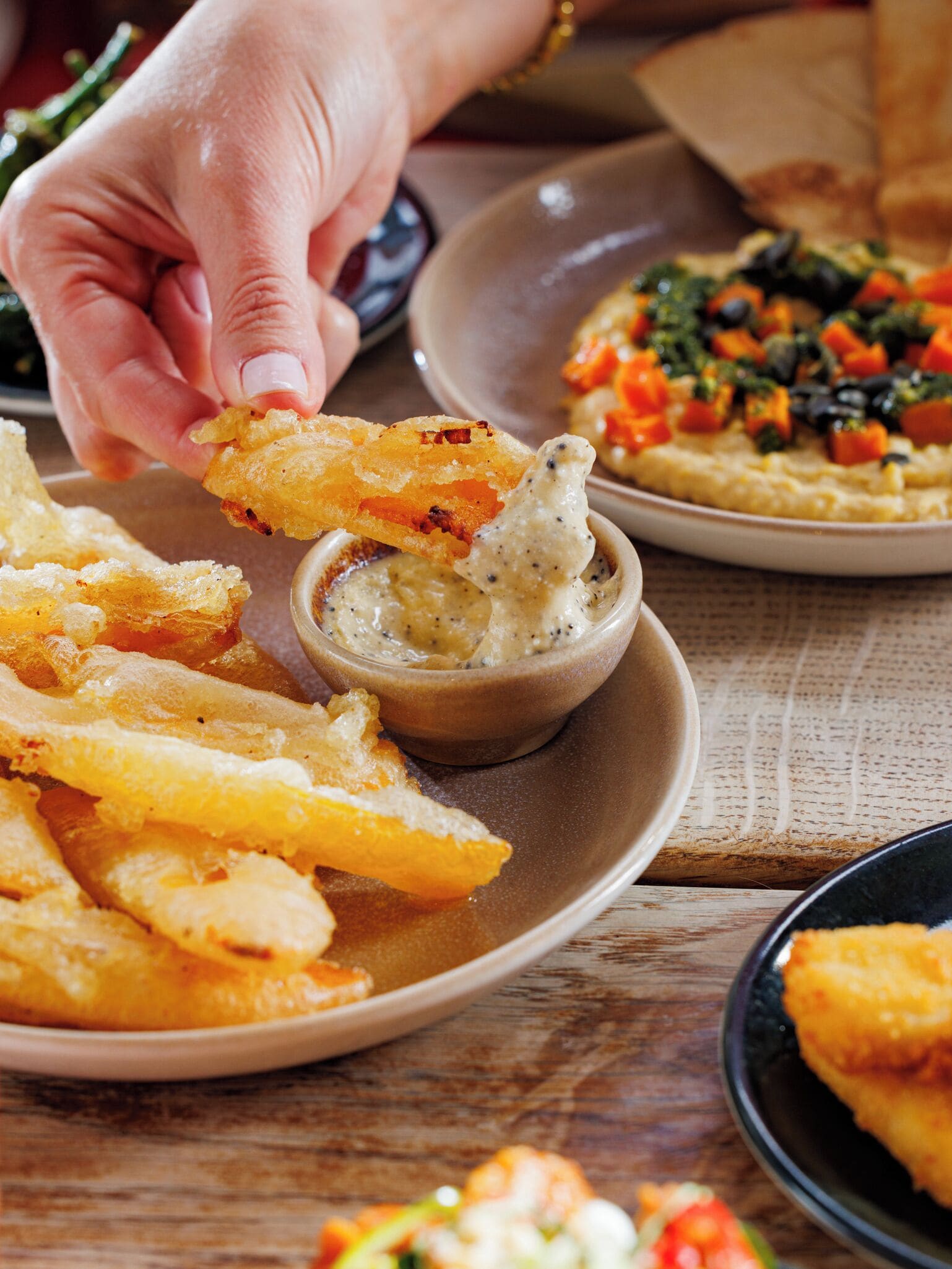 A hand dipping a fried item into a bowl of sauce.