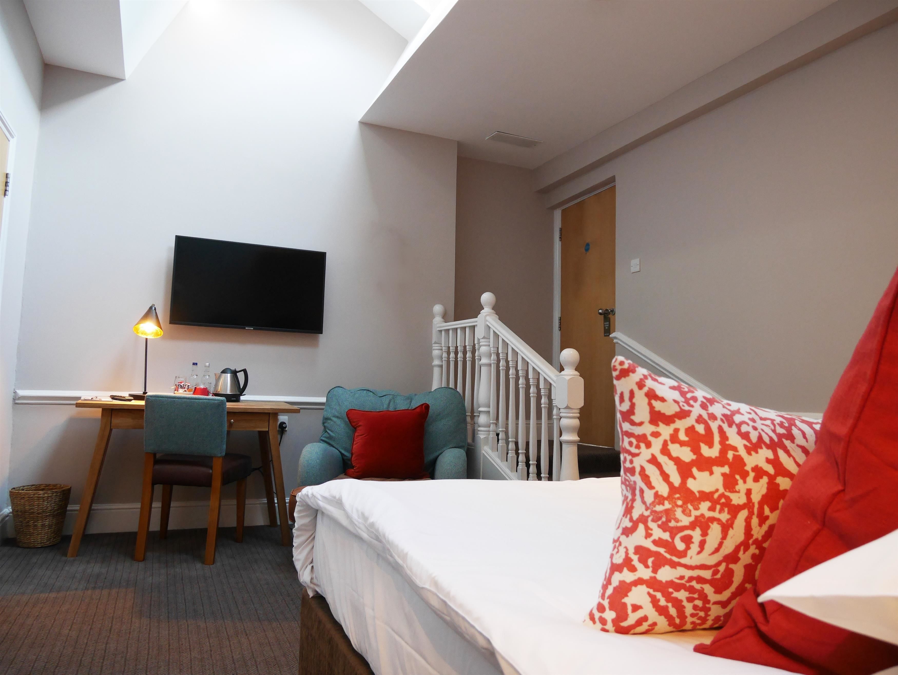 A bedroom with a bed, a desk with a chair, a television, and a staircase.