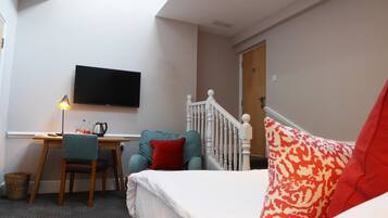A bedroom with a bed, a desk with a chair, a television, and a staircase.