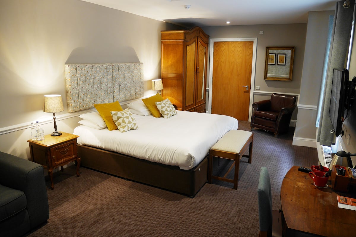 A hotel room with a large bed, bedside tables, a desk, a chair, and a wardrobe.
