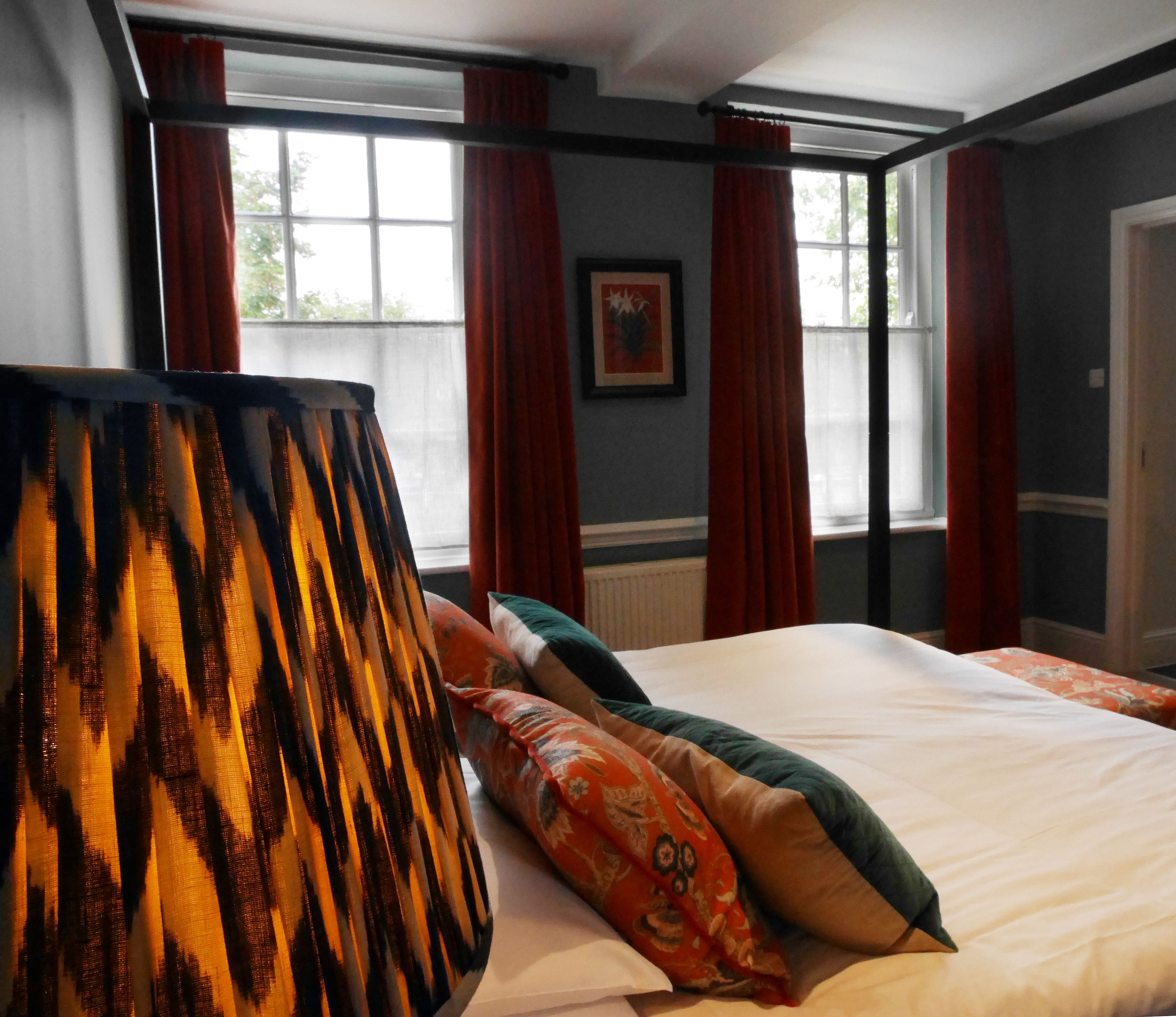 A hotel room with a large bed, red curtains, and a window with a view of trees.