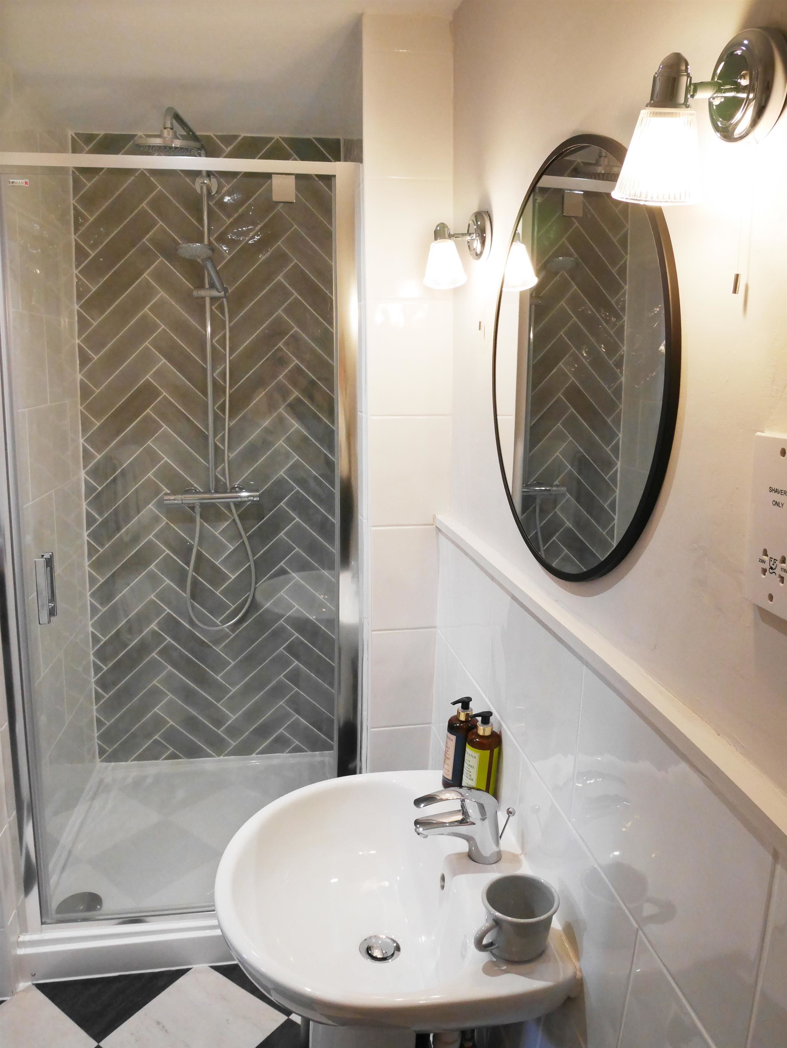 Un bagno con doccia vetrata, lavandino bianco e specchio tondo.