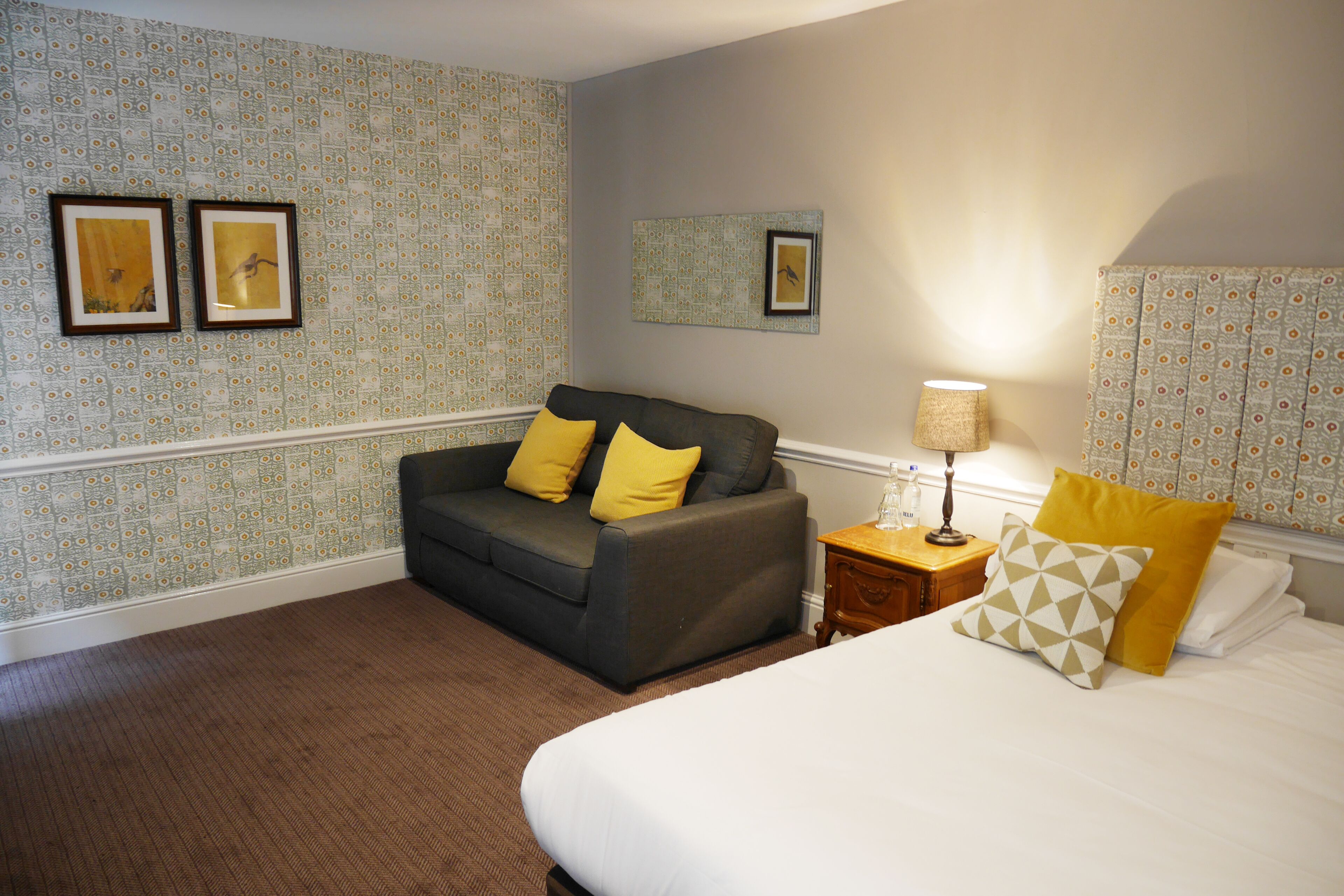 A hotel room with a bed, a sofa, a nightstand, and a lamp.