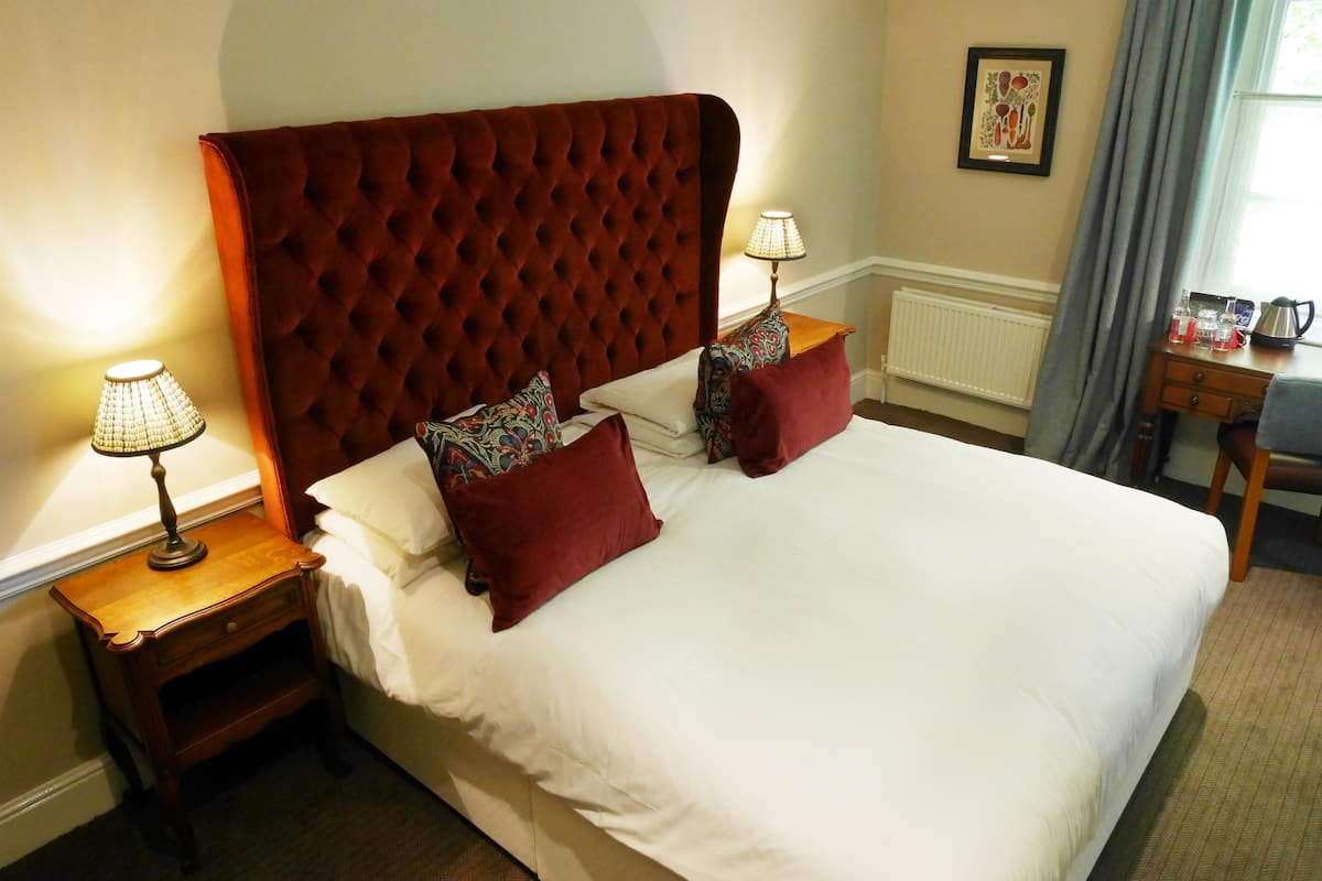 A neatly made bed with a tufted headboard, two bedside tables with lamps, and a small wooden side table with a kettle.