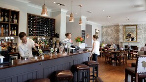 A bar area with a bartender, a wine rack, and a seating area with tables and chairs. - The Fleece (Witney)
