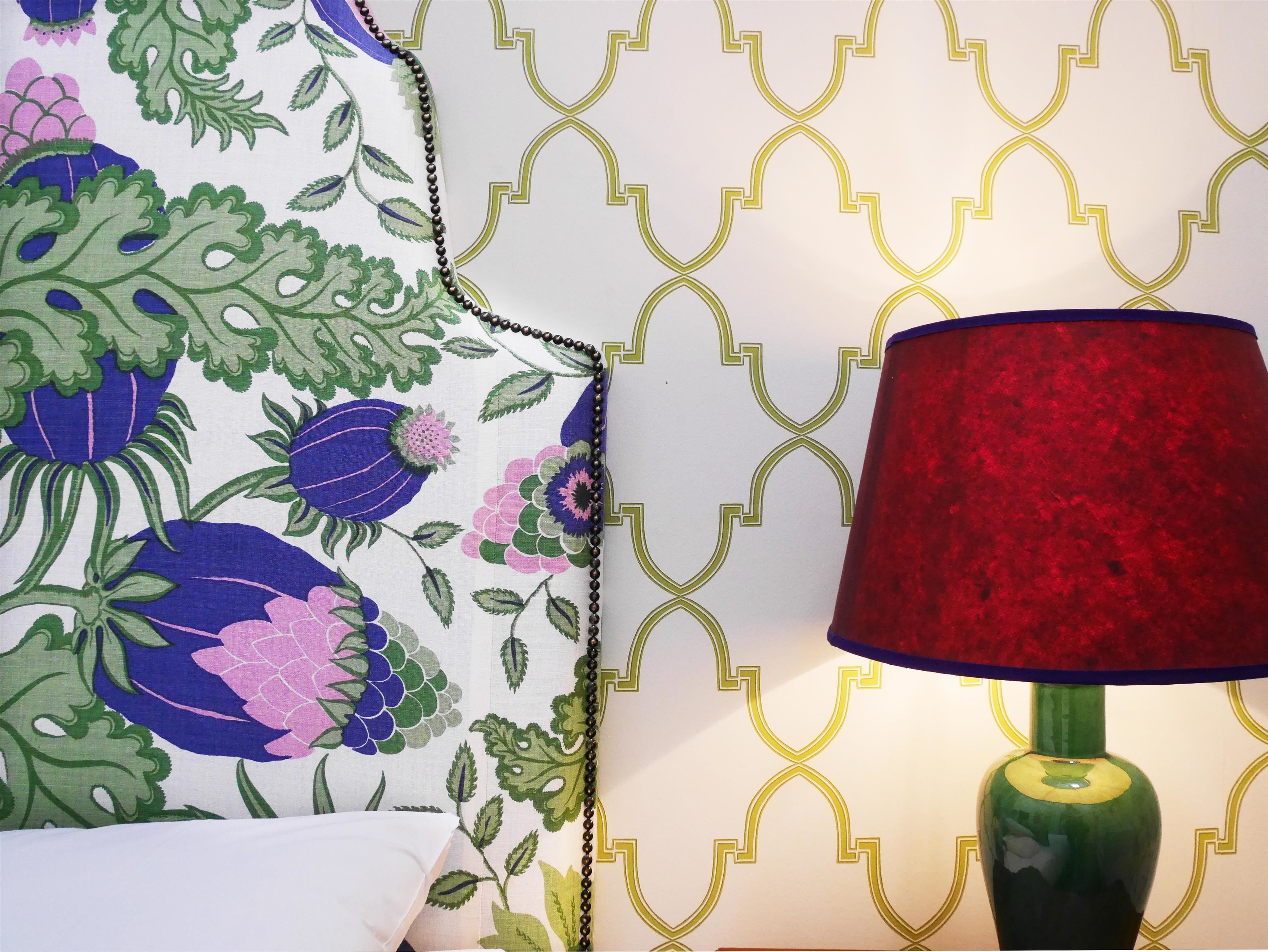 A bed with a floral-patterned bedspread and a green lamp with a red shade.