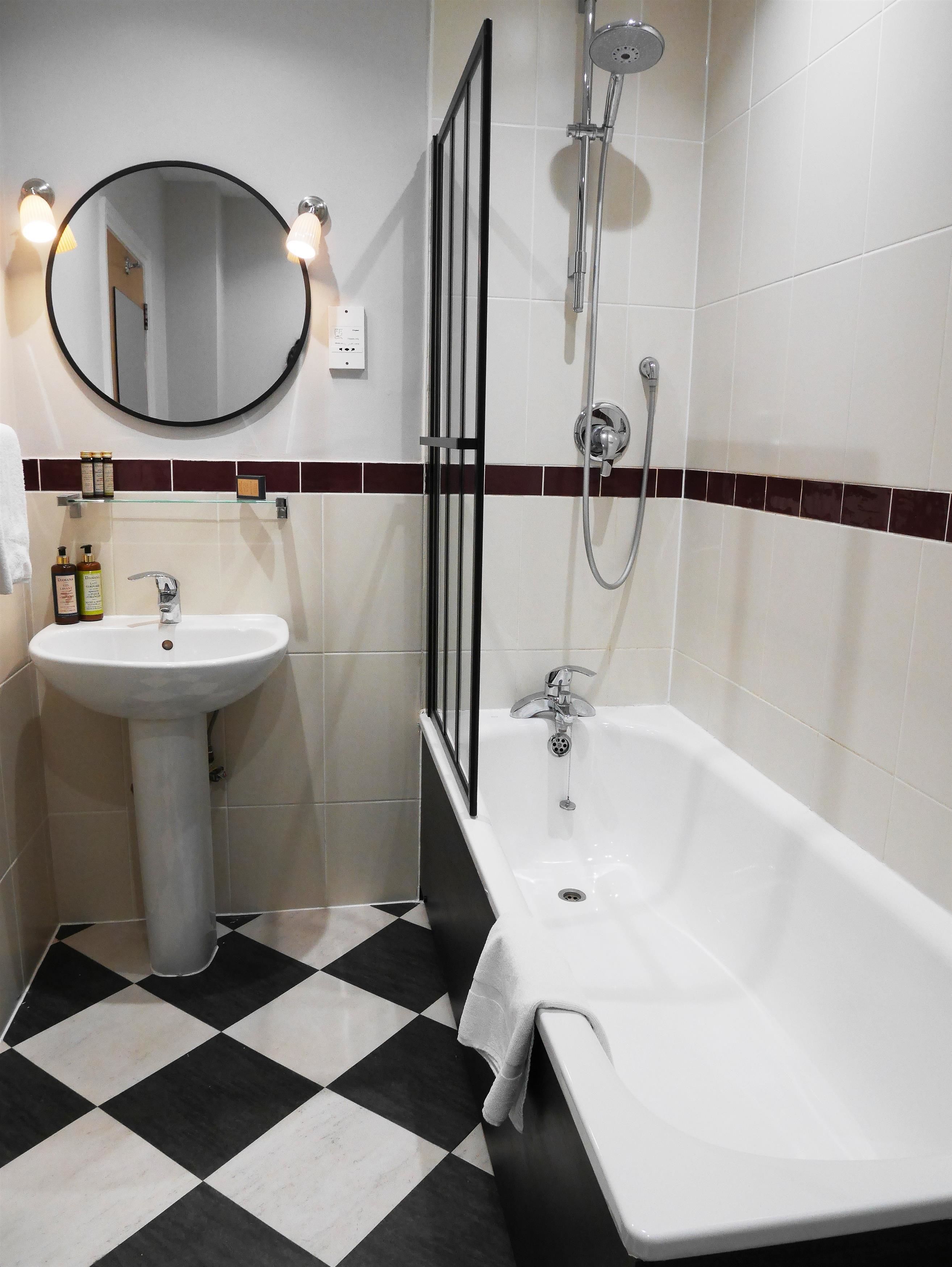 Ein Badezimmer mit einem weißen Waschbecken, einem runden Spiegel, einer Badewanne und einer Dusche.