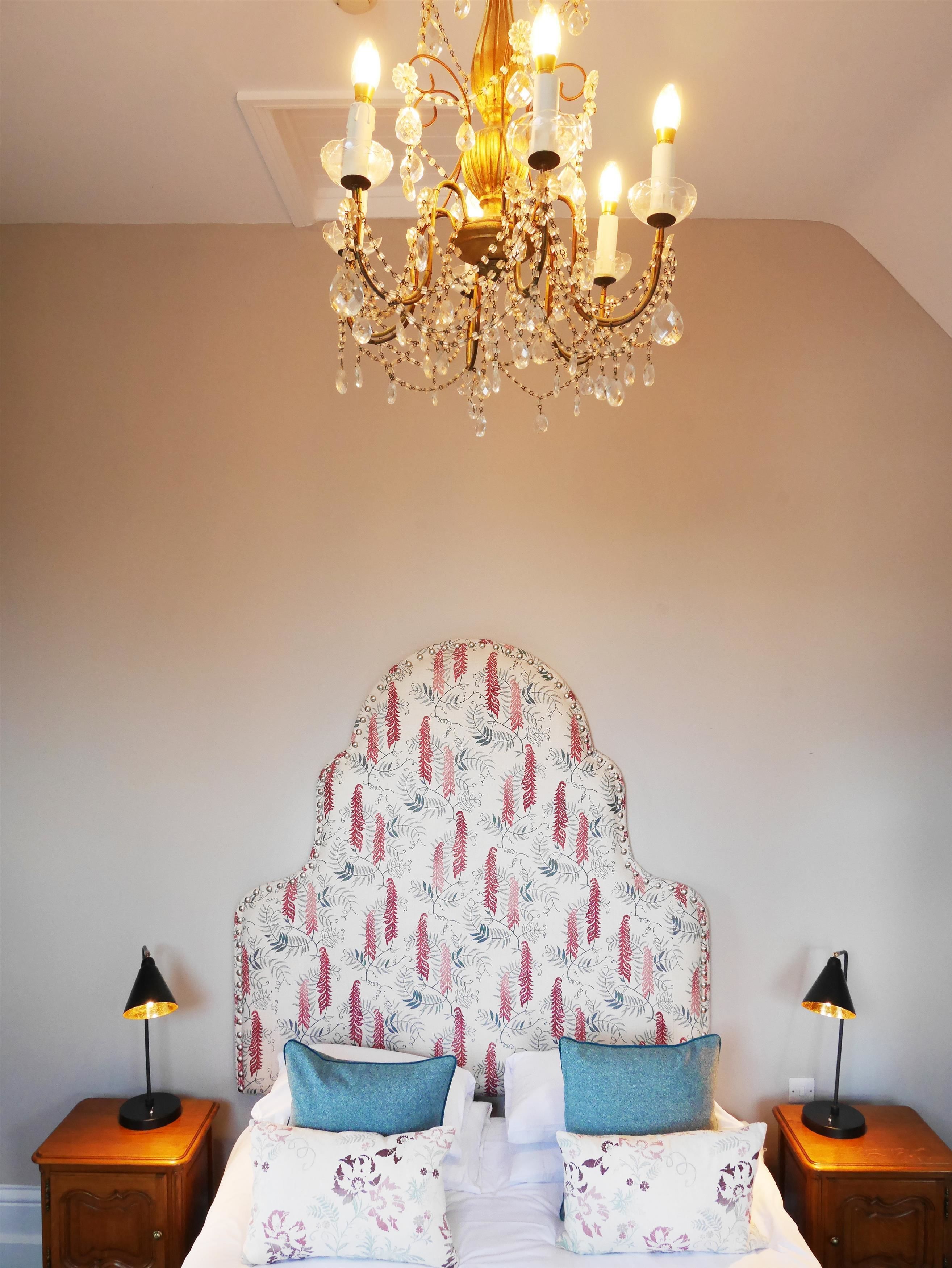 A bedroom with a large, ornate chandelier, a floral-patterned headboard, and two bedside tables with lamps.