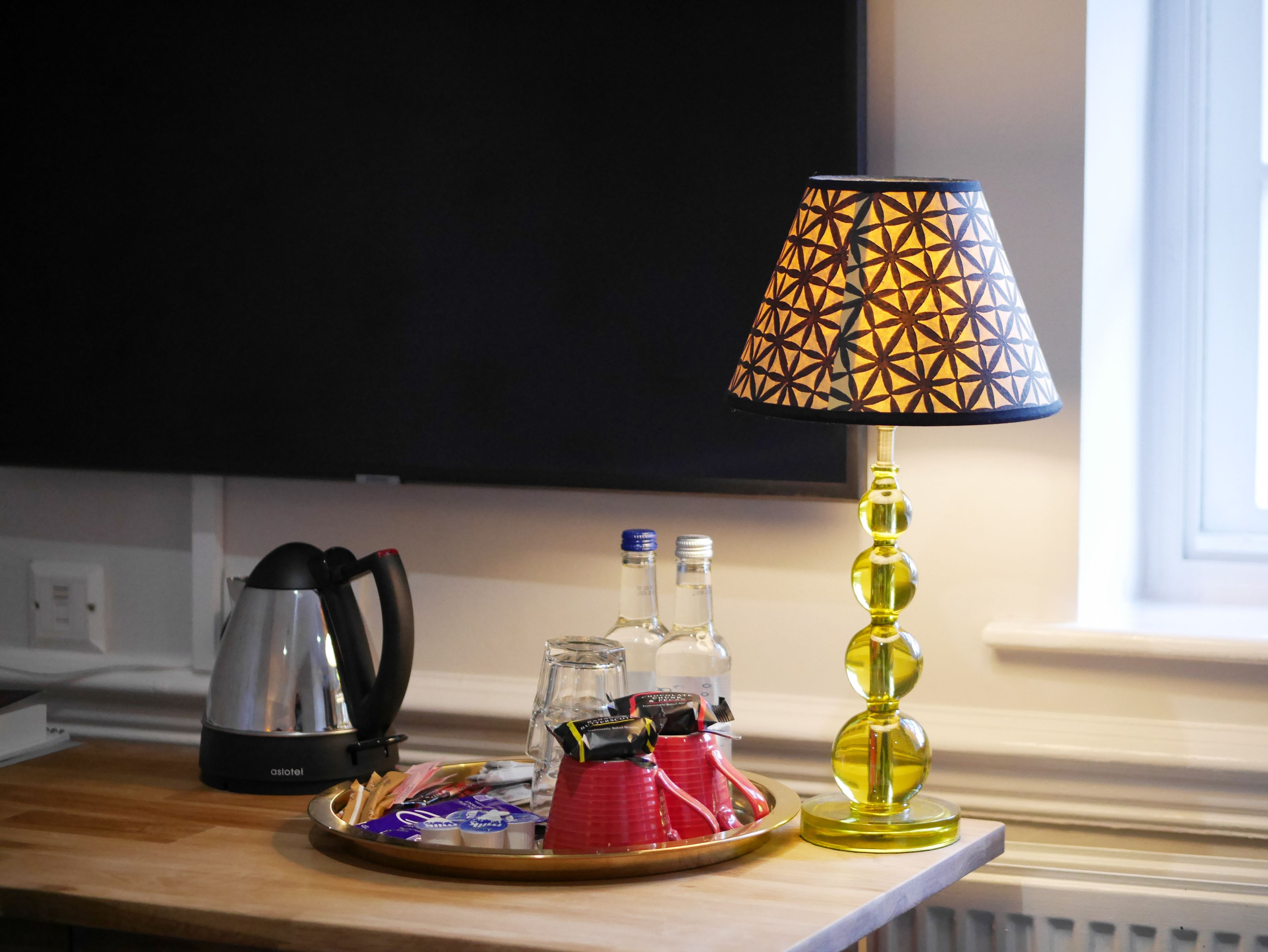 Una mesa con una bandeja de aperitivos, una cafetera y una lámpara decorativa.