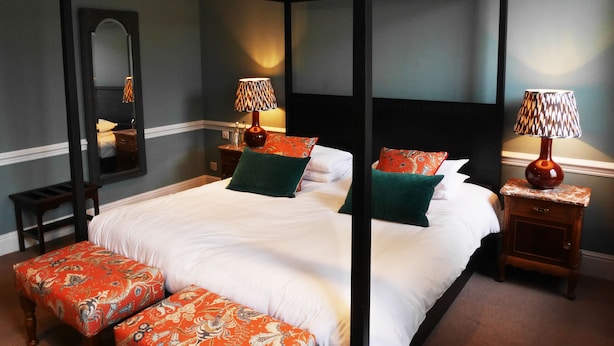 A four-poster bed with white linens, two bedside tables with lamps, and a bench with patterned cushions. - The Fleece (Witney)