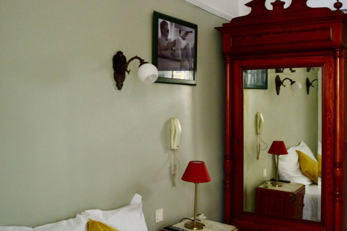 Habitación de hotel con cama, mesita de noche, lámpara roja, espejo y un cuadro en la pared.