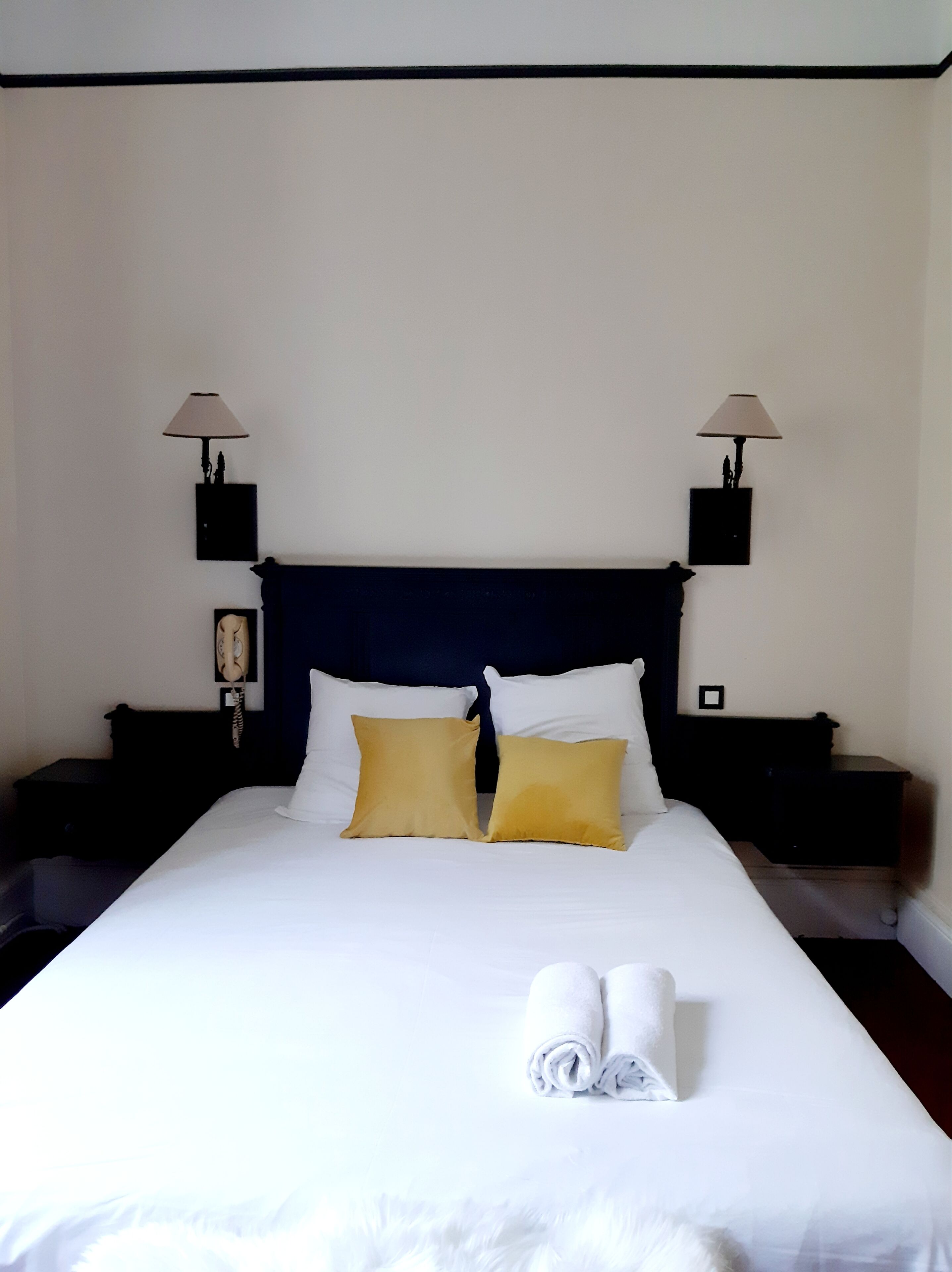 A neatly made bed with white and yellow pillows, a dark headboard, and two bedside tables with lamps.