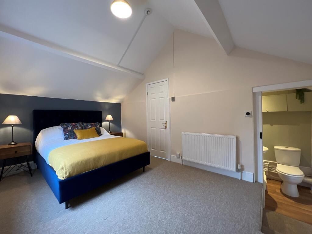 A bedroom with a bed, bedside tables, a radiator, a door, and a bathroom with a toilet.