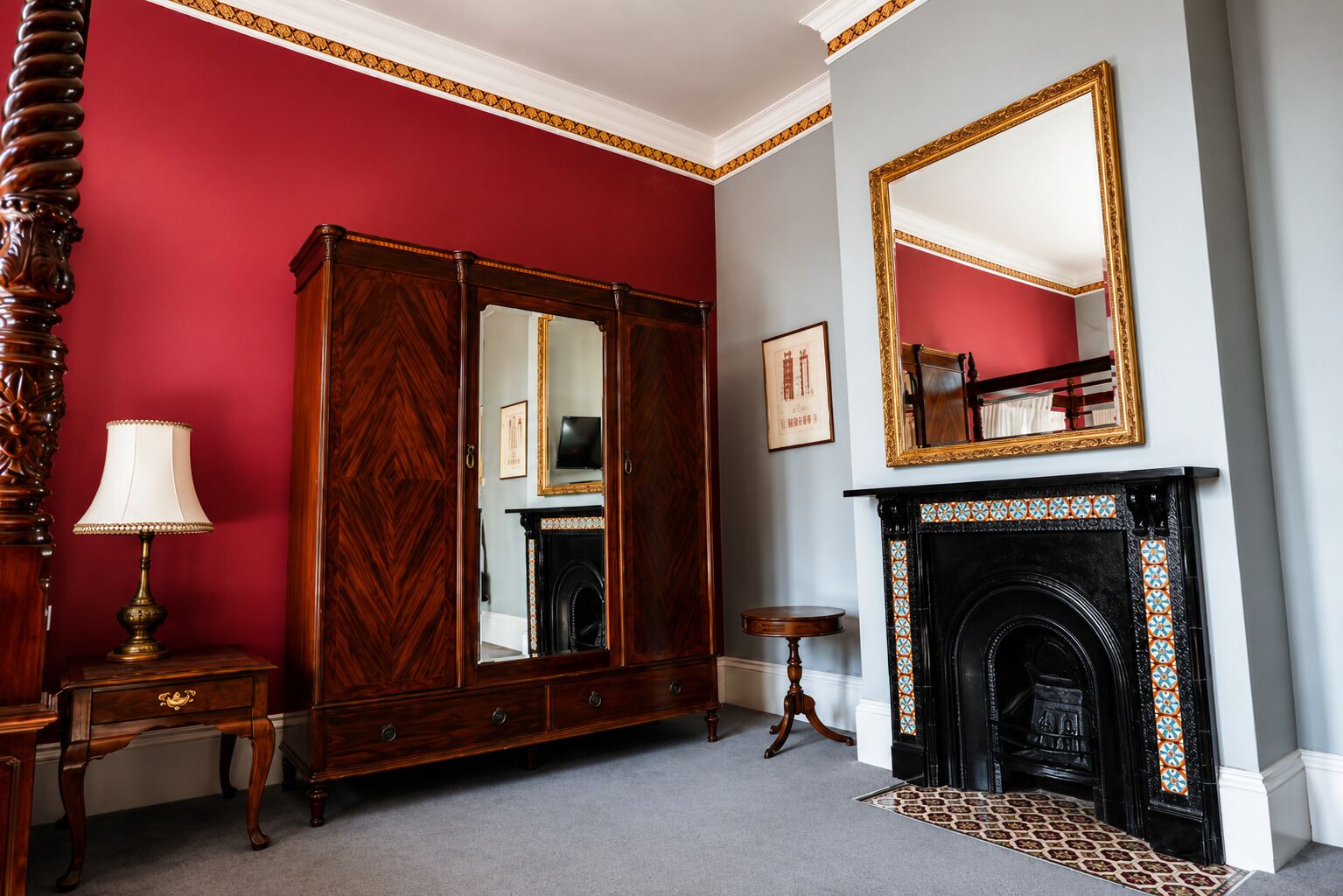 Una habitación con una pared roja, un espejo grande, una chimenea y un armario de madera.