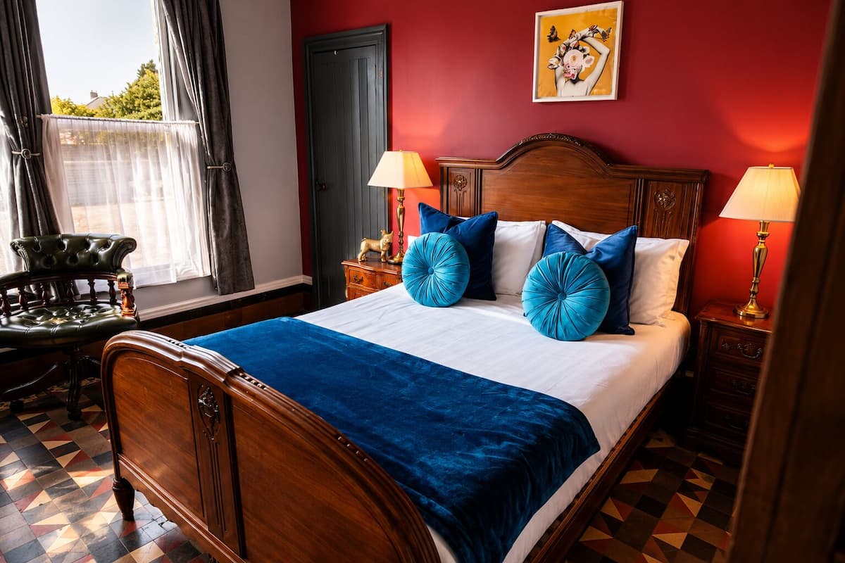 A room with a bed, two bedside tables, a chair, a window with curtains, and a door.