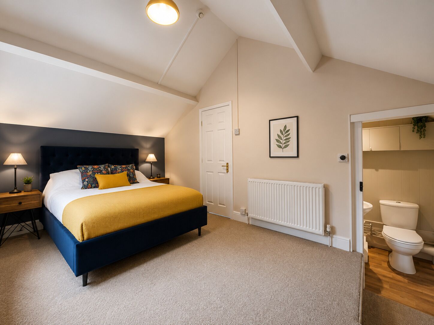 A bedroom with a bed, bedside tables, a radiator, a door, and a bathroom with a toilet.
