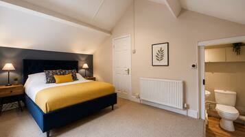 A bedroom with a bed, bedside tables, a radiator, a door, and a bathroom with a toilet.