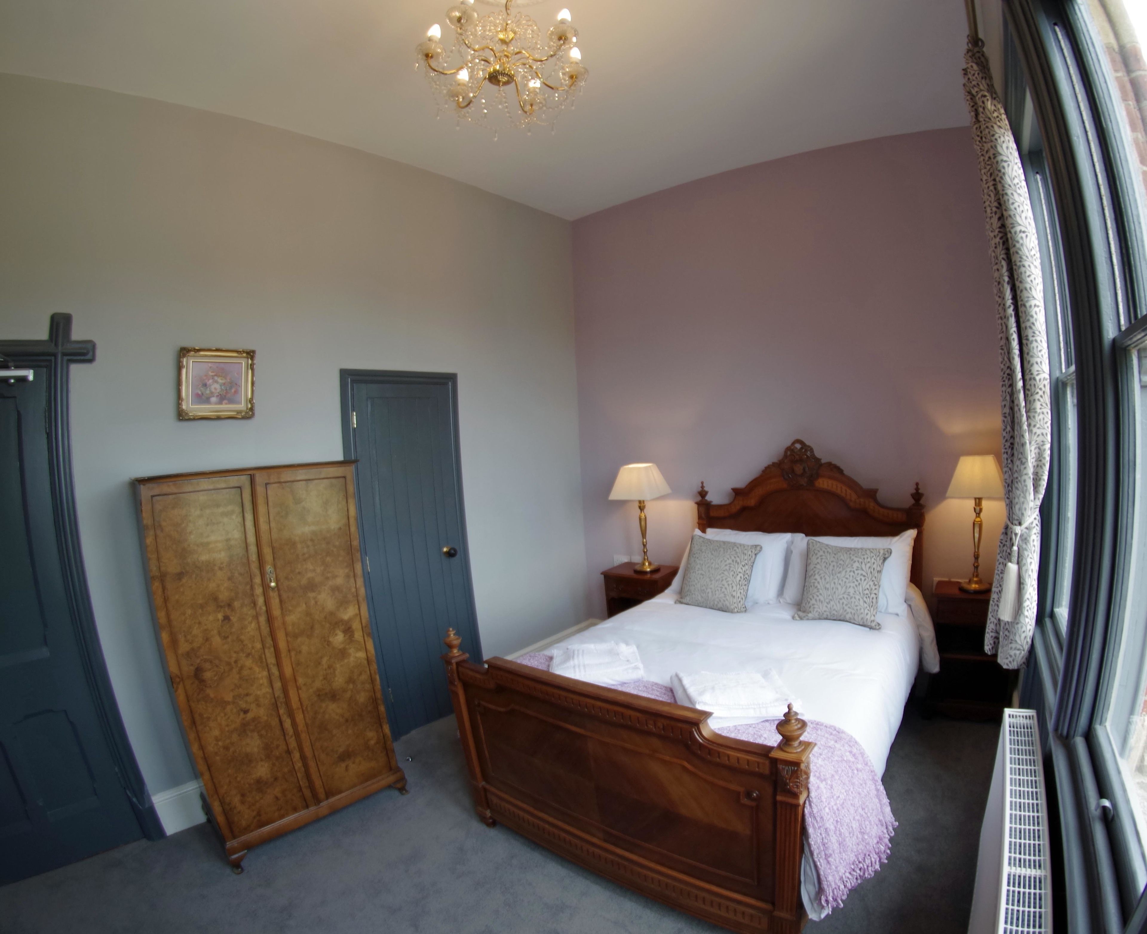 A bedroom with a wooden bed, two bedside tables with lamps, a wardrobe, a door, and a radiator.