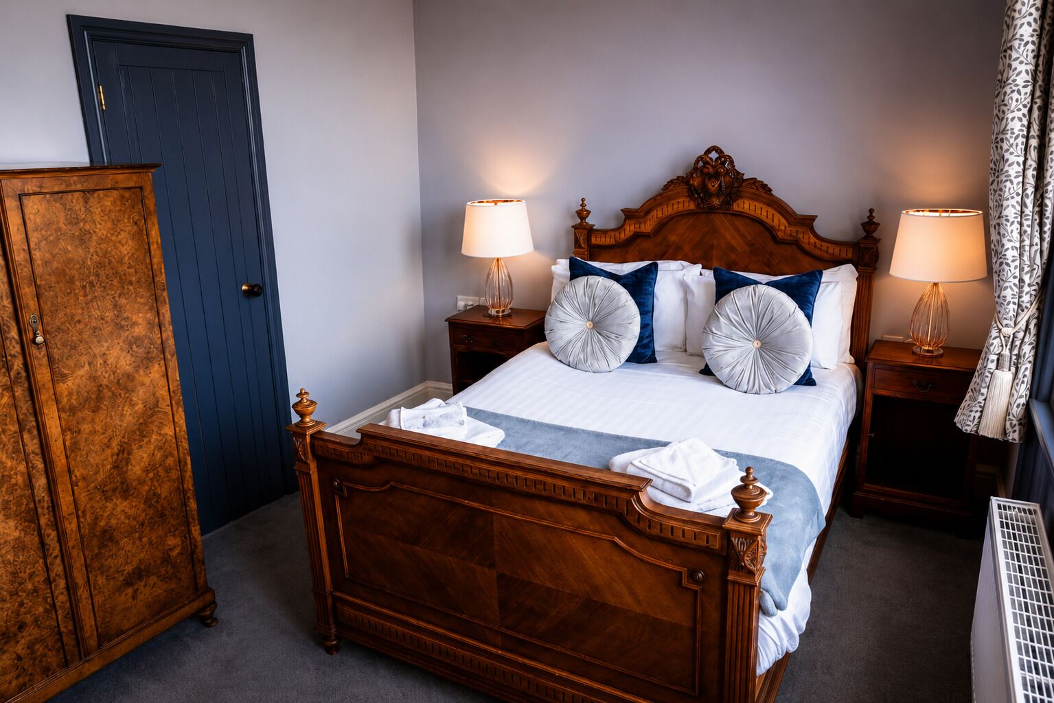 A wooden four-poster bed with white linens, two bedside lamps, and decorative pillows.