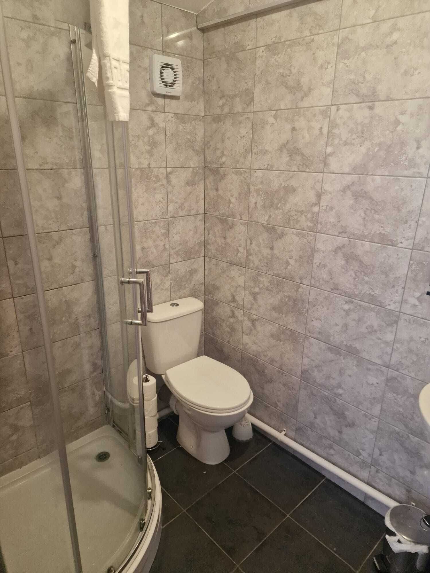 Een badkamer met een douchecabine van glas, een toilet en een kleine prullenbak.