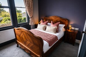 Quarto com cama de madeira, mesa de cabeceira, janela com cortinas e vista para o verde lá fora.
