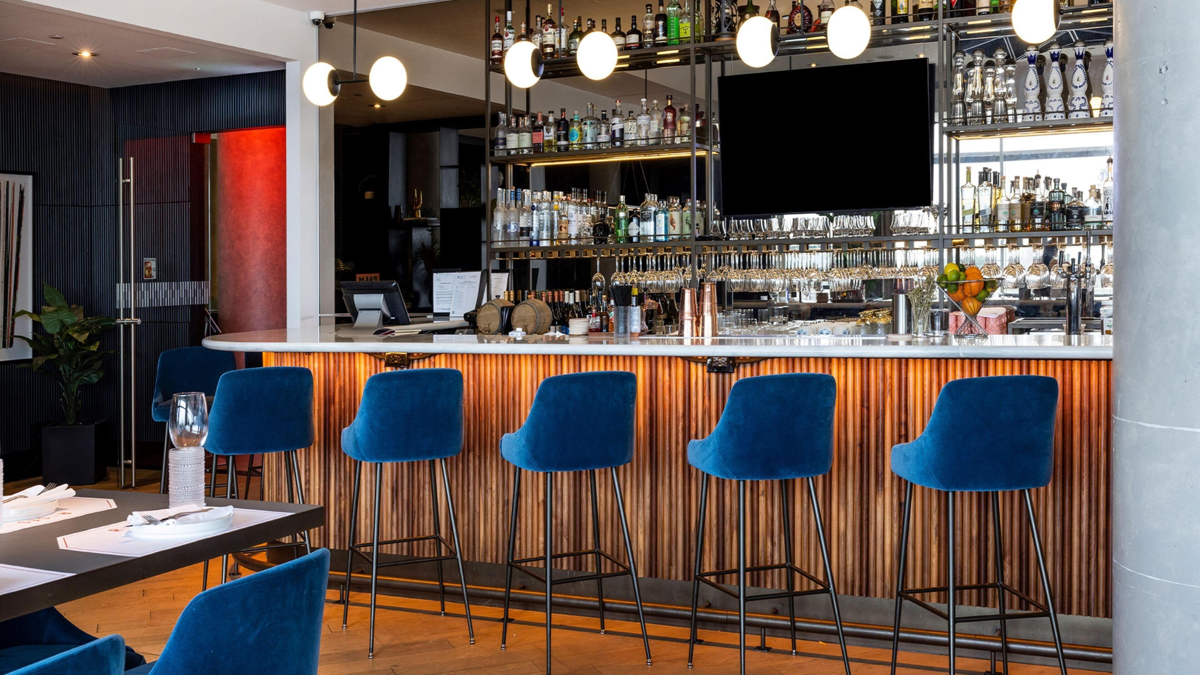 Een bar met een toonbank, krukken en verschillende flessen en glazen.